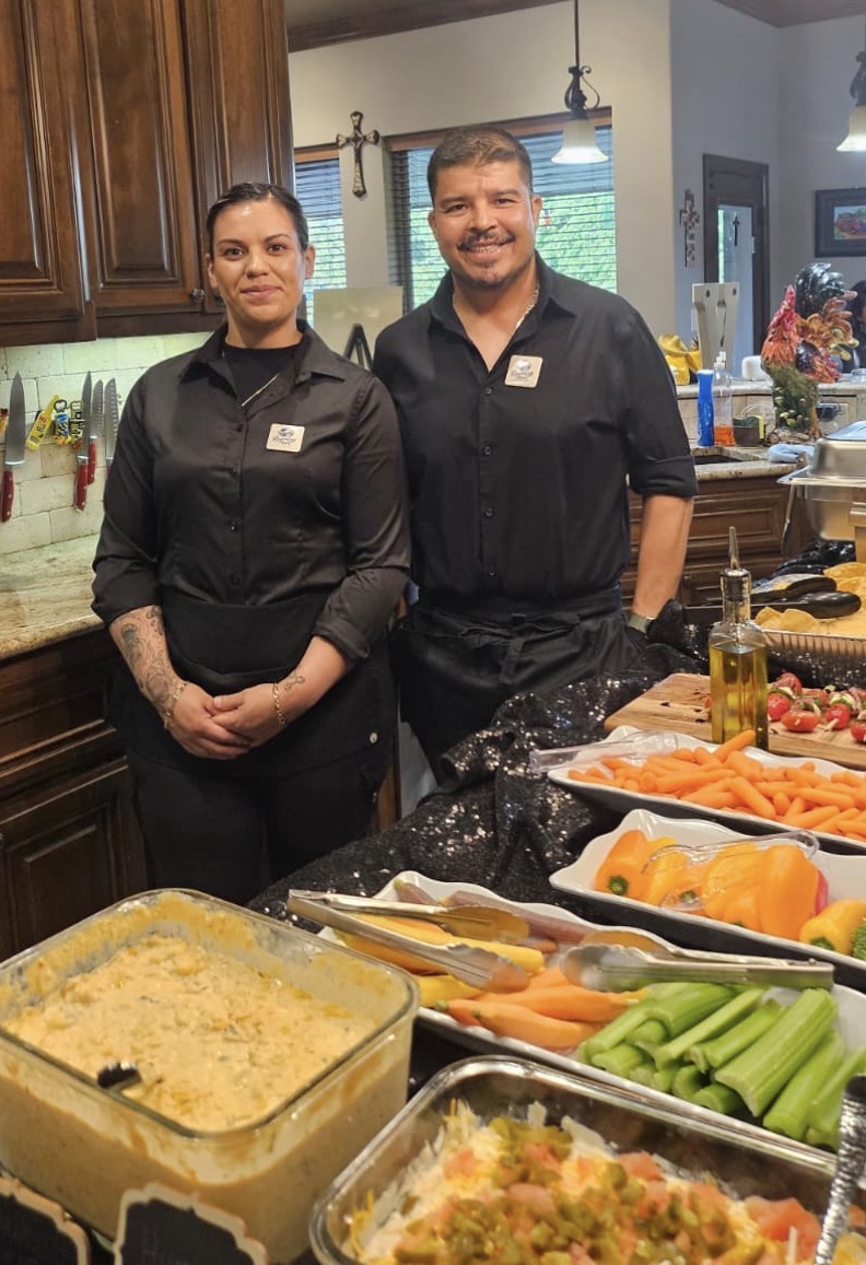 The founder and a team member in a kitchen surrounded by prepared food trays and fresh ingredients