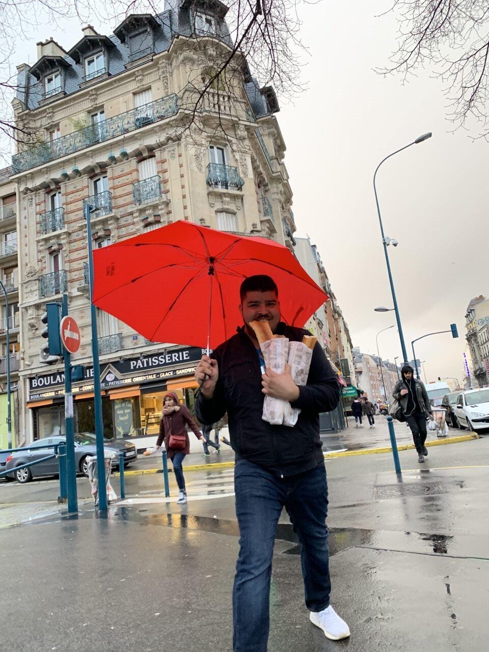 The founder walking a rainy Paris street with a red umbrella and fresh baguettes