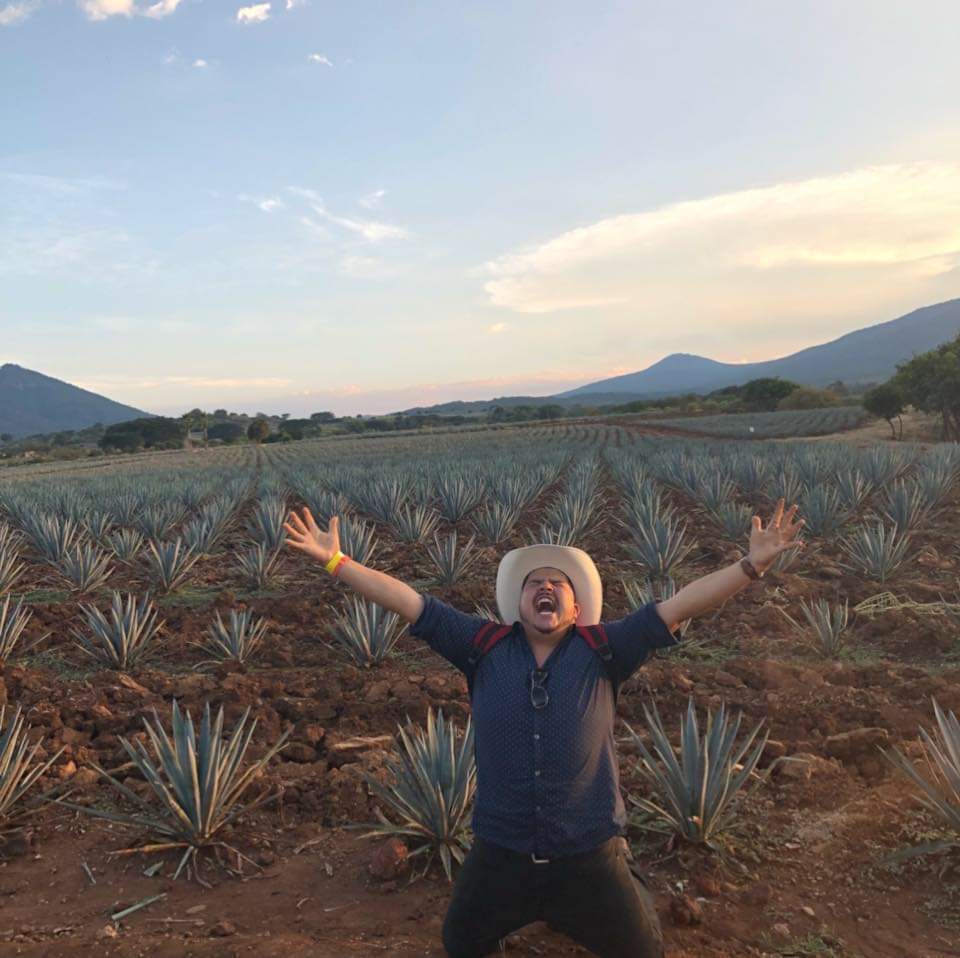 The founder standing with arms outstretched in an agave field in Mexico